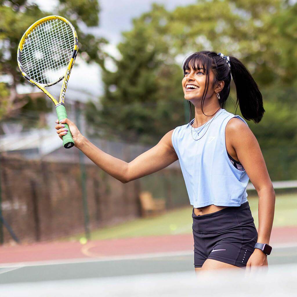 Smiling woman practicing tennis with a racket during summer in a training session on an outdoor court.