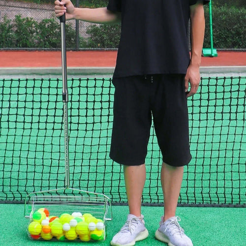 Adjustable tennis ball picker held by a person near a tennis court net, collecting colorful tennis balls.