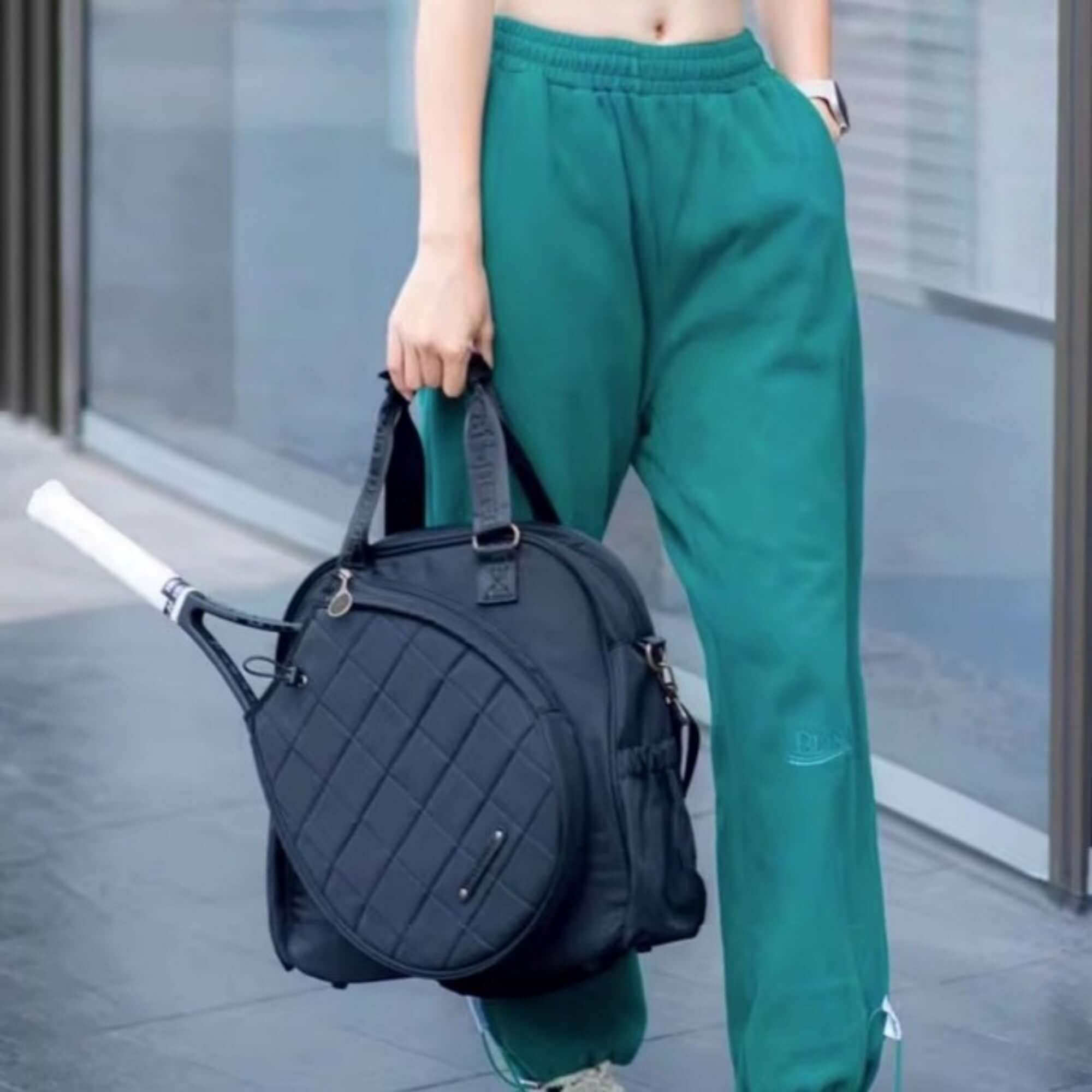 Person holding a stylish tennis and badminton bag set while wearing green athletic pants.