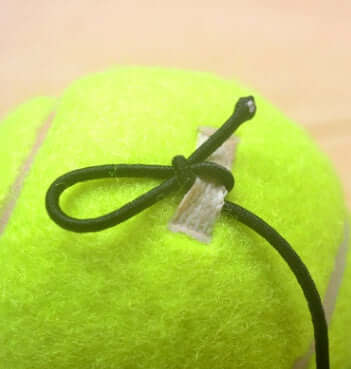 Tennis with Tennis String showing a close-up of the compact tennis training aid with string attached.